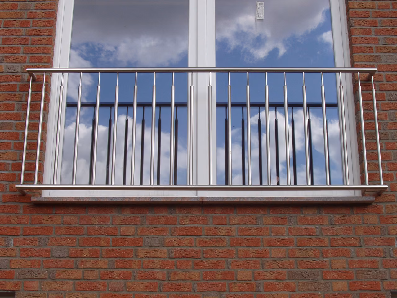 Französischer Balkon aus Edelstahl vor einem Fenster in einer Klinkerfassade